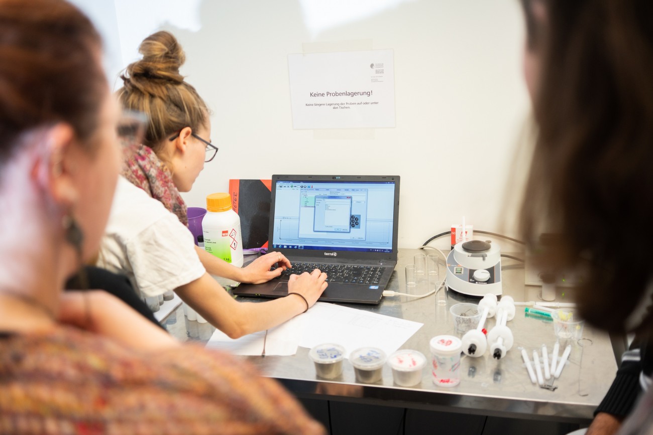 Studierende vor einem Laptop auf einem Tisch mit Probenbehältern